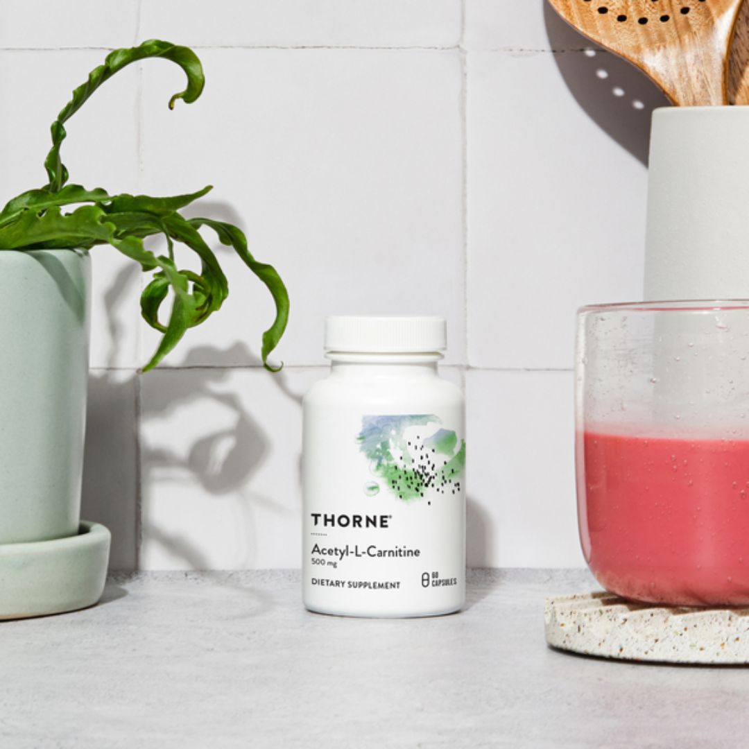 Thorne supplement bottle on a kitchen counter with a plant and glass of pink liquid in the background.