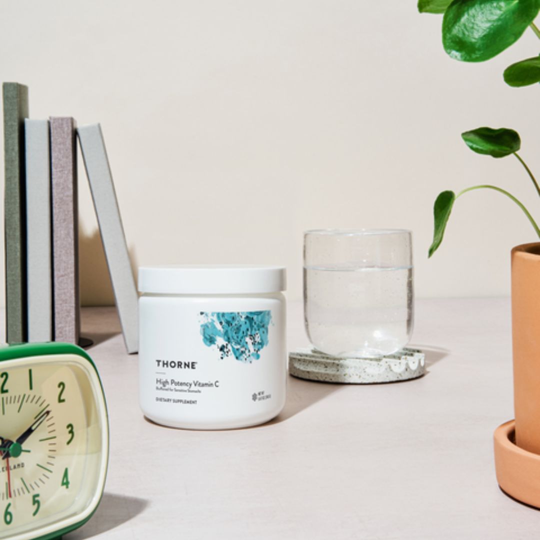 Thorne supplement container on a table with a glass of water, alarm clock, and books in the background.